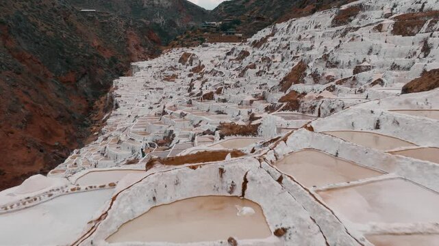 Drone aerial view of the historic Maras Salt Mines near Cusco, Peru. Thousands of terraced salt evaporation ponds cover the mountainside, creating a striking geometric pattern in the heart of the Sacr