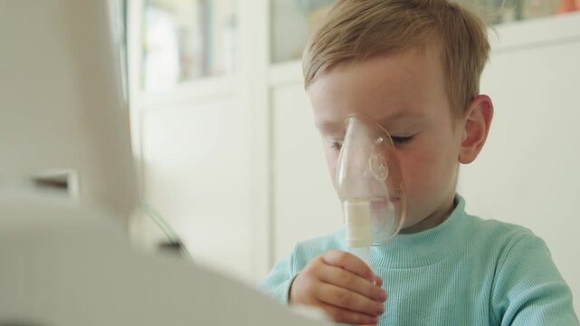 Boy getting respiratory treatment through a nebulizer mask. Child with an illness inhaling medicine through a nebulizer mask, inhalation therapy. Sick kid using an inhalator for cough, nursing and res