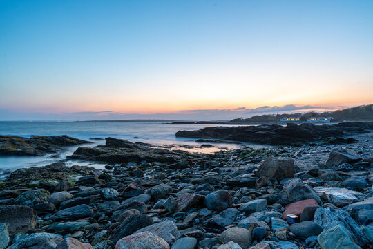 Newport rocky coastline at twilight, a sunset long-exposure landscape showing a boulder-strewn shore and smooth ocean waves under a pastel sunset sky in Newport, Rhode Island.