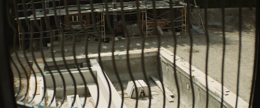 Concrete foundation and structural framework at an active construction site viewed through metal fencing during a modern building development project.