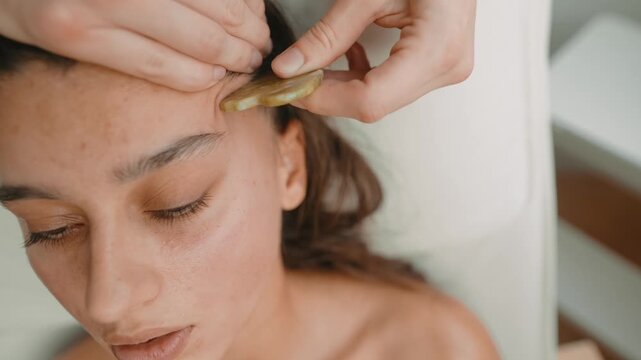 Aesthetician carefully shaping eyebrows using jade stone tools