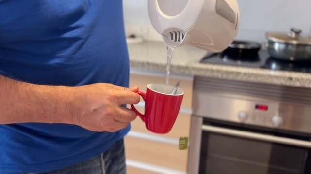 Hombre vertiendo agua caliente en una taza de t&eacute; en la cocina