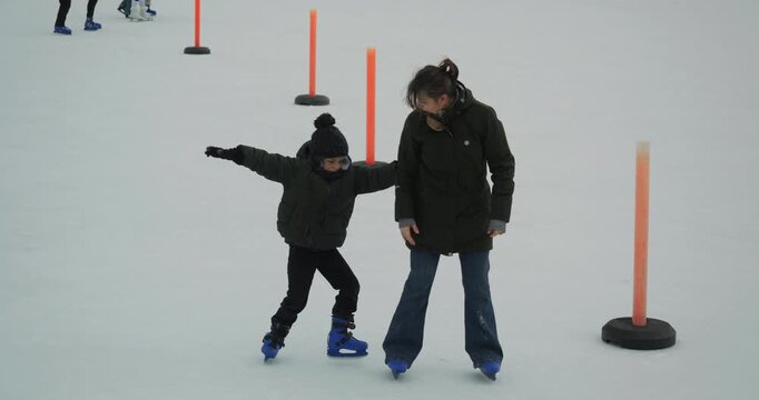 Mother helps her little son to learn the ice skating on rink