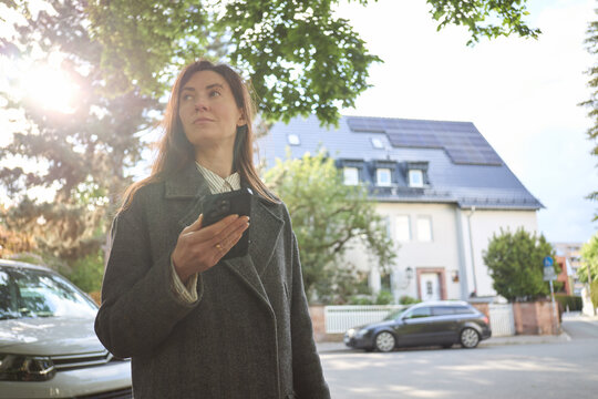Woman holding smartphone in front of a house with solar panels on the roof