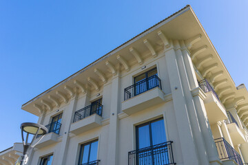 Classical style residential building featuring elegant beige facade, decorative cornices, and wrought iron balconies against a clear blue sky in bright daylight © John_Doo78