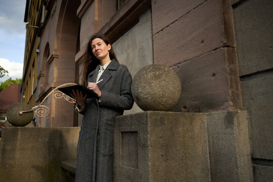 Woman in coat using tablet near stone spheres outside old building