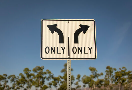 A traffic sign with arrows indicating that one can turn only left ot right against a blue sky