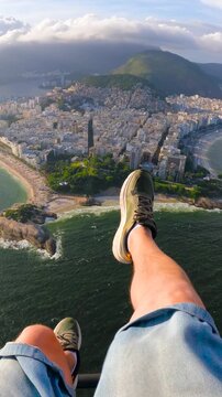 POV view of a young man paragliding over the urban coastline, Arpoador rock, and the Atlantic Ocean in Rio de Janeiro, Brazil.