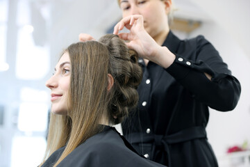 Fototapeta premium Stylist styling woman's hair in beauty salon, selective focus