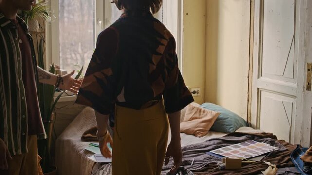 Tilt down shot of gen Z Caucasian woman arguing with tattooed boyfriend about cluttered bed covered with clothes, food and other stuff in shared apartment during heated domestic conflict