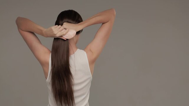 Dark-haired woman combing her long shiny straight hair on gray background.