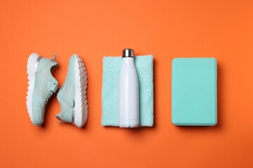 Obraz premium Sports equipment. Foam block, water bottle, towel and sneakers on orange background, flat lay
