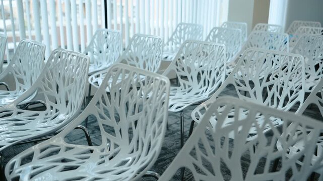 Modern conference room with rows of white designer chairs featuring abstract tree branch patterns, arranged for a meeting, seminar, or presentation in a contemporary office interior.