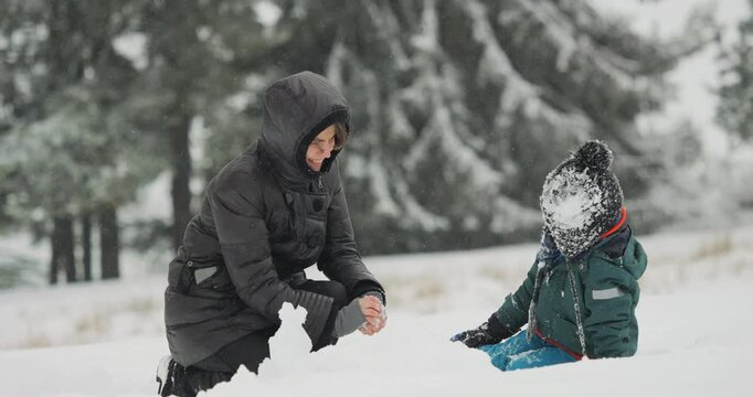 Mother and child kneeling together in deep snow, playing and packing snow while enjoying a winter day outdoors
