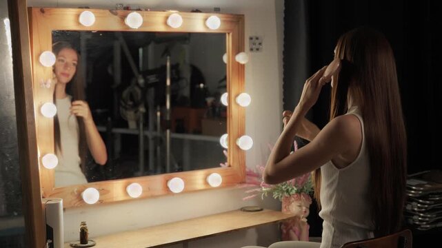 A woman with long brown hair combs her hair while seeing her reflection in the mirror