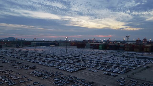 Wide dusk aerial view of vehicle export terminal and container port near coastline