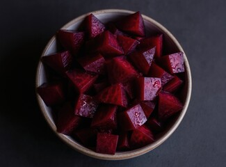 Obraz na płótnie Canvas Bowl with diced cooked beets. Deep red vegetable pieces glistening with moisture on dark textured surface. Minimalist food presentation for healthy eating.