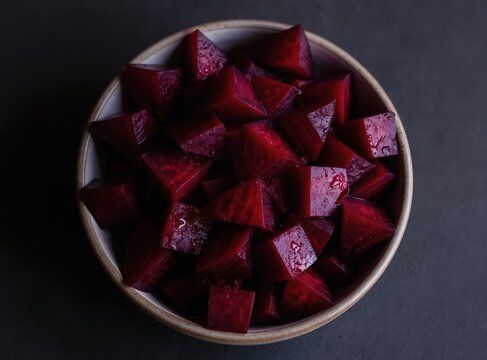 Bowl with diced cooked beets. Deep red vegetable pieces glistening with moisture on dark textured surface. Minimalist food presentation for healthy eating.