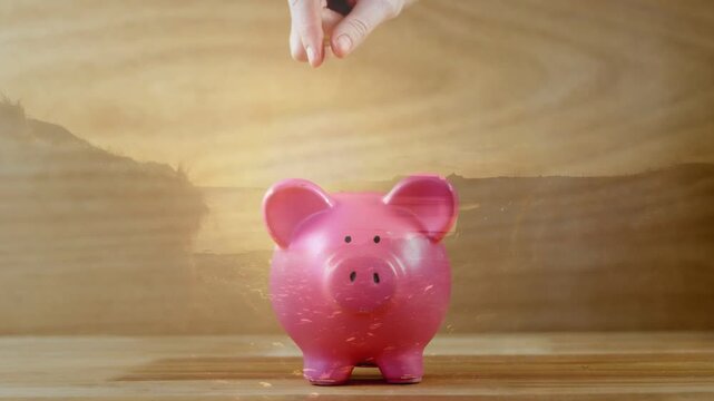 Human hand entering, lowering and releasing coin over pink piggy, coin ricocheting left for saving