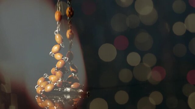 Rosary strand released from above, descending on glossy surface, beads tumbling forming mirror pile