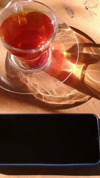 Vertical video: Tilting camera revealing glass cup on saucer on table sun moving caustics and phone