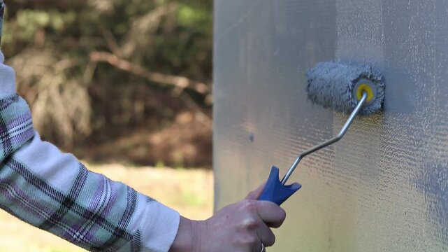 Painting a wall with a roller in gray. The process of applying gray paint to the surface using a paint roller. The master's hand applies a layer of gray paint to the wall using a textured paint roller
