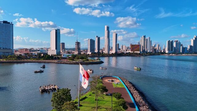 Panama flag and city skyline near waterfront. Panama flag in foreground, boats on bay, skyline and waterfront park under blue sky from elevated angle
