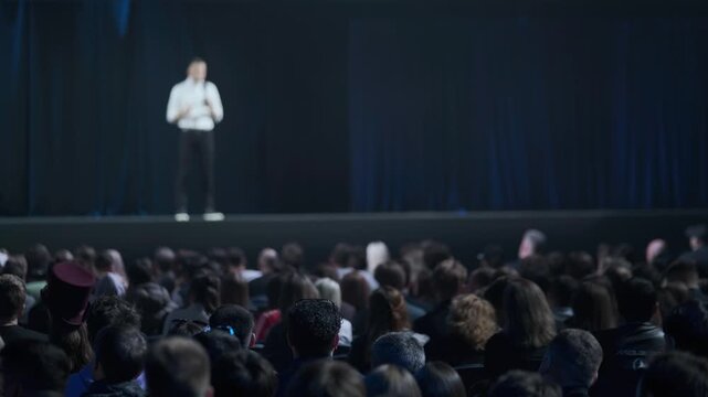 Crowd focused on keynote speaker on stage at large conference, professional atmosphere, networking, learning, engagement.