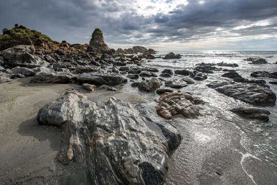Rocky coast, rocks on the beach, dark rain clouds, long time exposure, West Coast, South Island, New Zealand