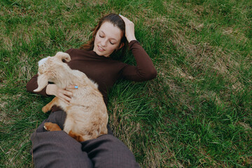 Obraz premium Relaxed woman lies on green grass outdoors, cuddling a young goat kid, sharing a gentle moment of companionship and calm, natural light, casual lifestyle scene with soft shadows, breeze, rural