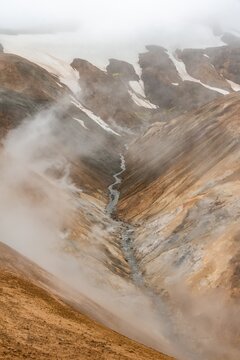 Steaming stream between colourful rhyolite mountains and snowfields, Hveradalir geothermal area, Kerlingarfj&ouml;ll, Icelandic Highlands, Iceland