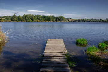 Naklejka premium Calm lake with wooden pier and reeds at Pilská reservoir in Czech countryside