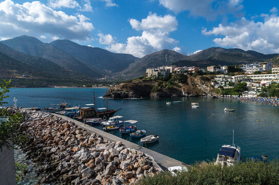 Beautiful coastal harbor with fishing boats, turquoise sea and mountain landscape on Crete island, Greece. Scenic Mediterranean bay with traditional boats, summer vacation destination.
