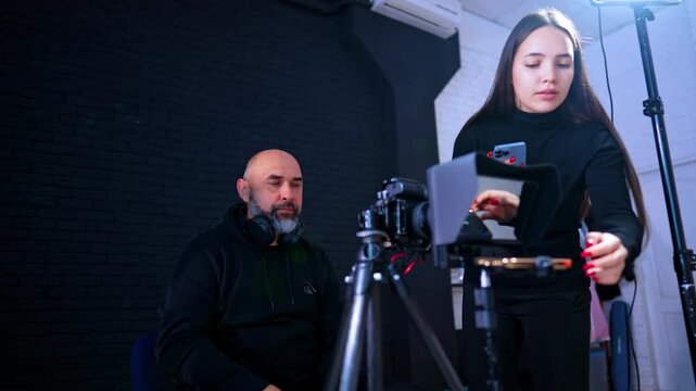 Crew adjusting teleprompter and camera settings in professional studio. Woman and man setting up camera and teleprompter equipment for video recording in a studio environment.