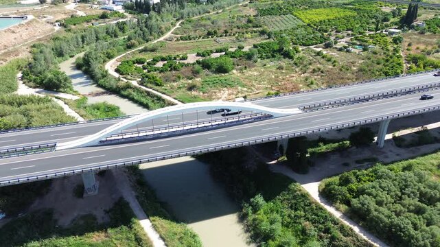 Aerial view of a modern highway bridge with a distinctive white arch crossing over the Segura river and the lush green fertile huerta of Murcia landscape during a sunny day