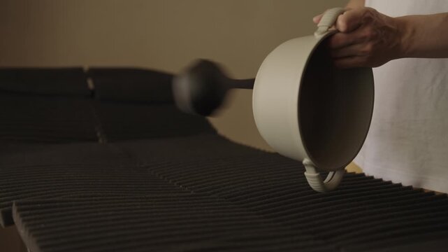 Man striking large pan with ladle to demonstrate sound absorbing properties of acoustic foam panels, concept of soundproofing technology and noise reduction materials in dark studio setting.