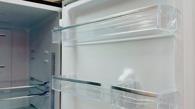 Close-up refrigerator door transparent shelves showing empty egg racks and small item bays, crisp white interior, sleek clear