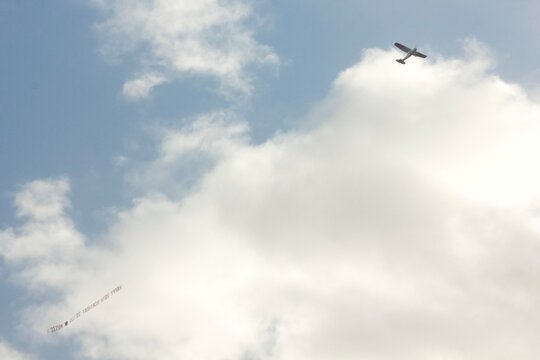 Airplane Flying With Banner In Front of Clouds