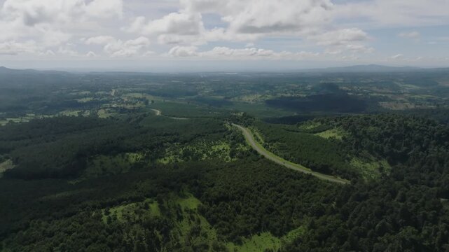 Aerial view of the lush Lembus Forest with a winding road cutting through dense green hills under a cloudy sky in Eldama Ravine, Baringo County, Kenya.