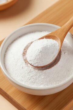 White tapioca starch powder is scooped from a bowl with a wooden spoon. The fine dry ingredient is prepared for cooking or baking in a kitchen.