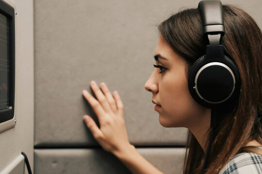 Young woman wears headphones during hearing test in clinic. Patient listens to sounds for audiometry exam. Doctor checks ear health with audiology equipment. Professional medical check-up for hearing.