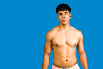 Fototapeta premium Young muscular man looking away on blue background