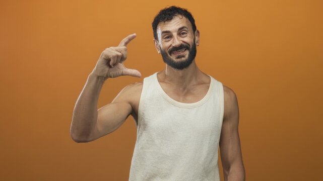 Man pinches a small gap with fingers and thumb in a studio orange backdrop, beard and tanktop visible; playful curiosity.