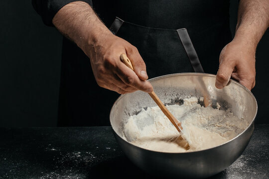 Professional baker mixing sourdough dough in metal bowl in dark kitchen for artisan bakery advertising