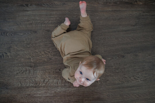 Top view of an infant lying on a dark wooden floor looking up at the camera