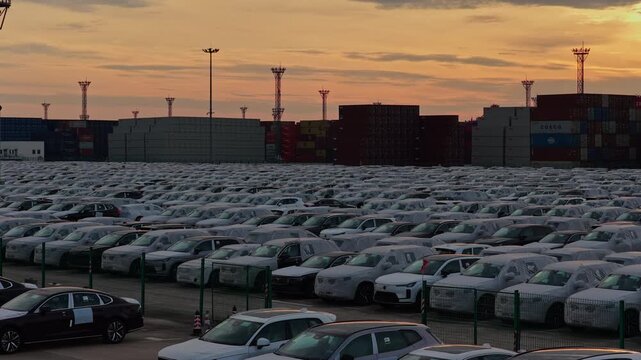 Automobile export yard with container stacks and sunset sky at industrial port
