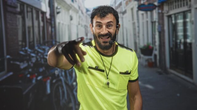 Man with whistle points finger forward on street wearing neon shirt and headset; crowd control vigilance.