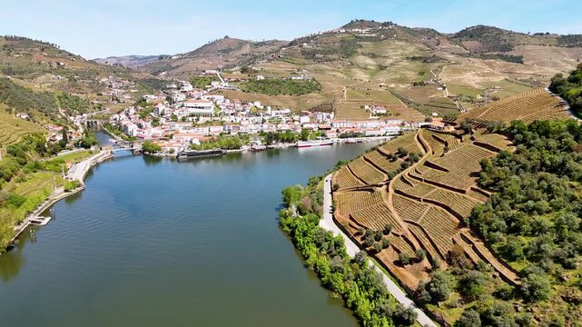 Aerial view of the Douro River flowing past the village of Pinhao and lush terraced vineyards under a clear blue sky Pinhao, Vila Real, Portugal.