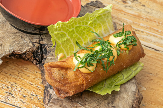 The photograph captures the glossy, slightly wrinkled texture of the rice paper wrapping a spring roll filled with shredded pork, bean sprouts, and Thai basil, illuminated by a soft central light.