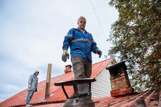 Chimney sweep working on house roof. Professional man repairing building ventilation system. Maintenance service for heater and fireplace. Construction worker fixing roof chimney exterior.